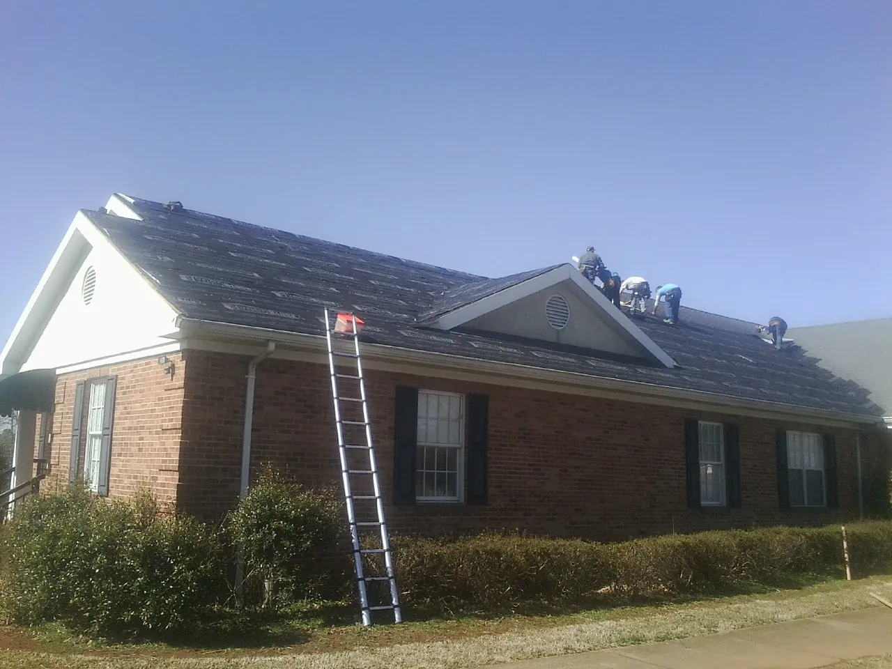 Crew tearing shingles off a brick ranch roof with a ladder set — Emergency Roof Repair work by our crew in Mokelumne Hill