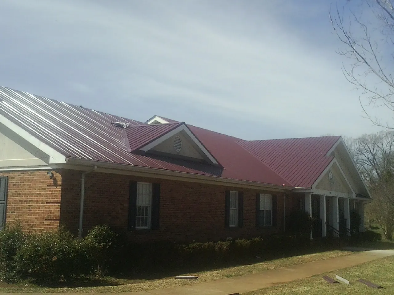 Red metal roof with gabled entries on a long brick building, from a Hail Damage Roof Repair job in Mokelumne Hill