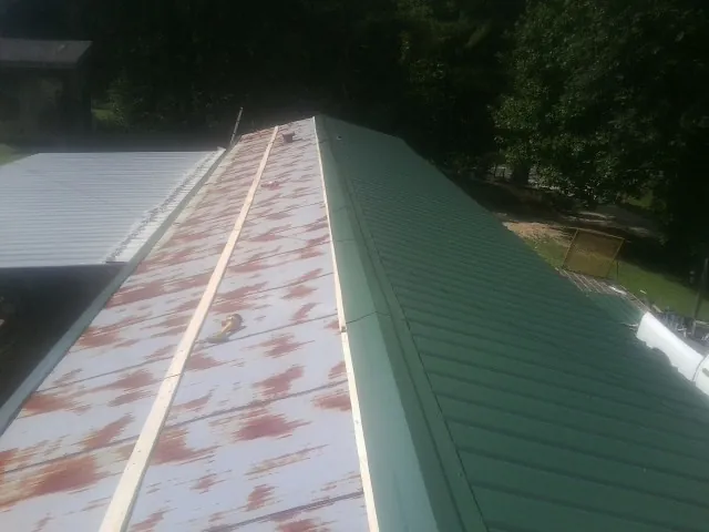 Old rusted panels beside newly installed green metal roofing — Wind Damage Roof Repair by Roofing Brothers in Mokelumne Hill