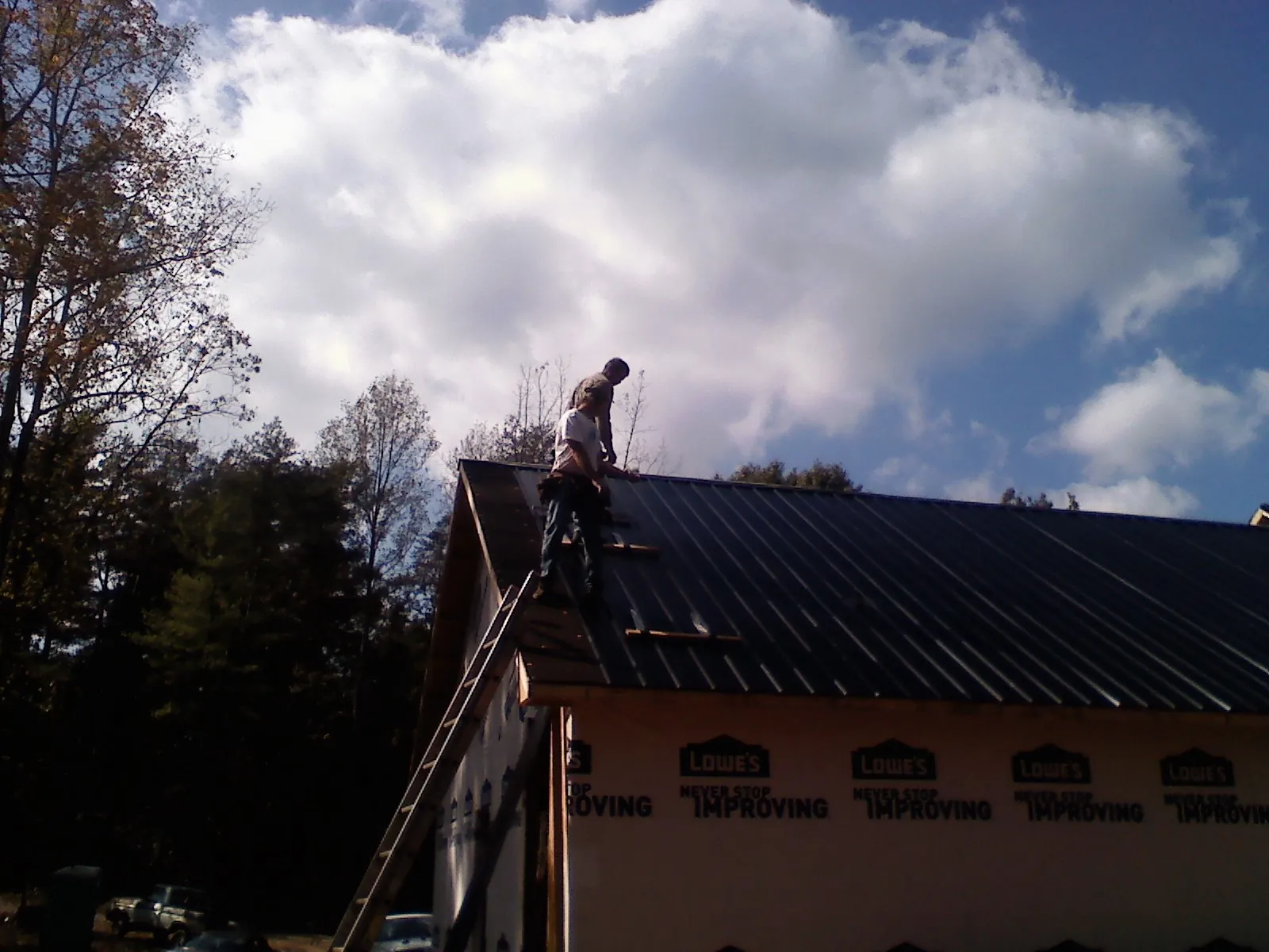 Roofer fastening dark metal panels high against a cloudy sky, from a Roof Inspection job in Mokelumne Hill