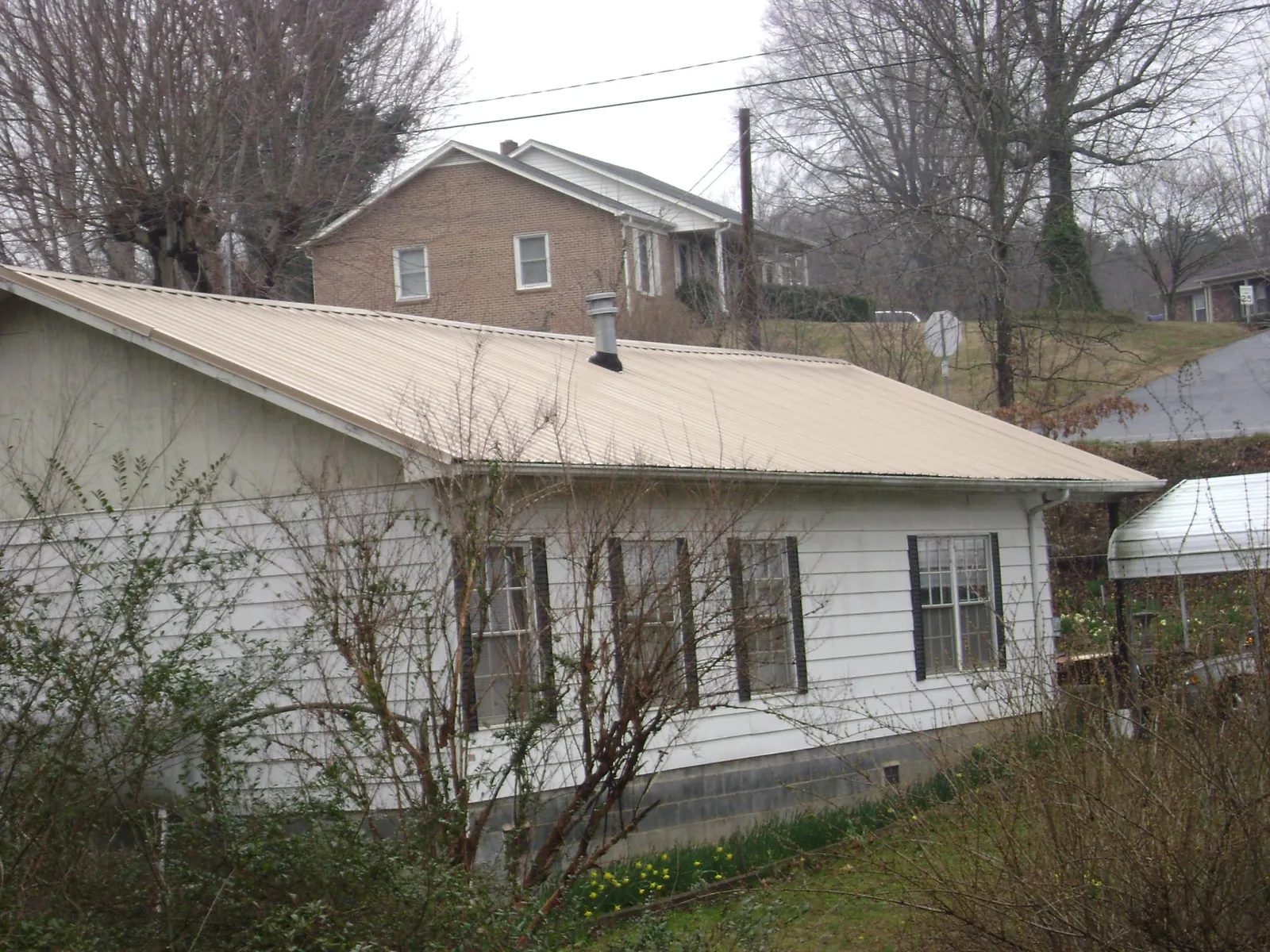 Tan metal roof on a white sided house set into a hillside — Commercial Roofing by Roofing Brothers in Mokelumne Hill